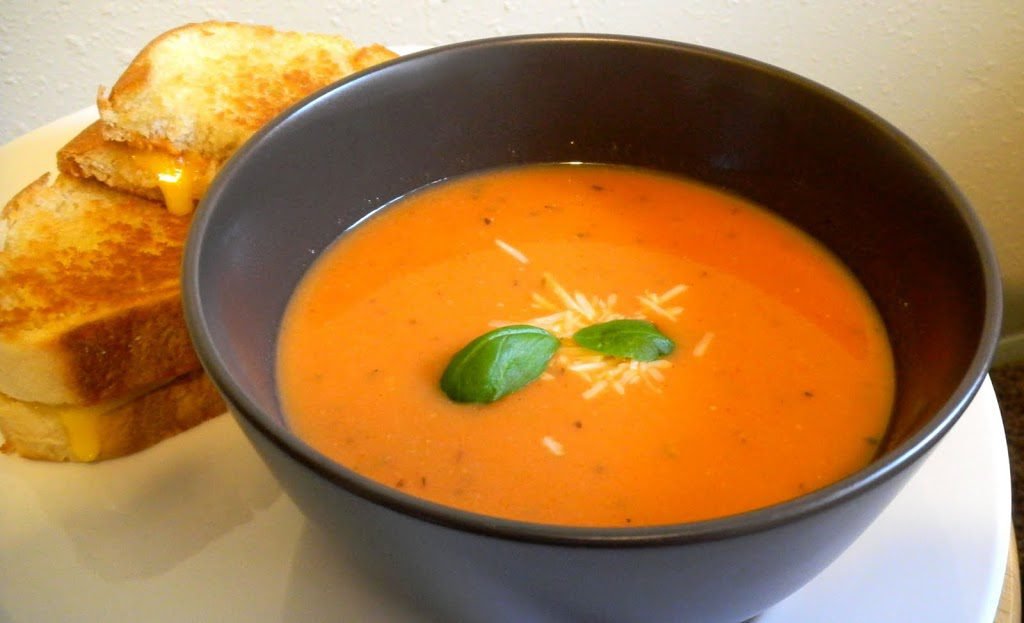 Bowl of tomato soup next to a grilled cheese sandwich