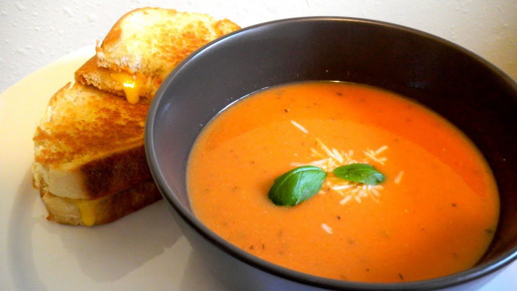 Bowl of tomato soup next to a grilled cheese sandwich