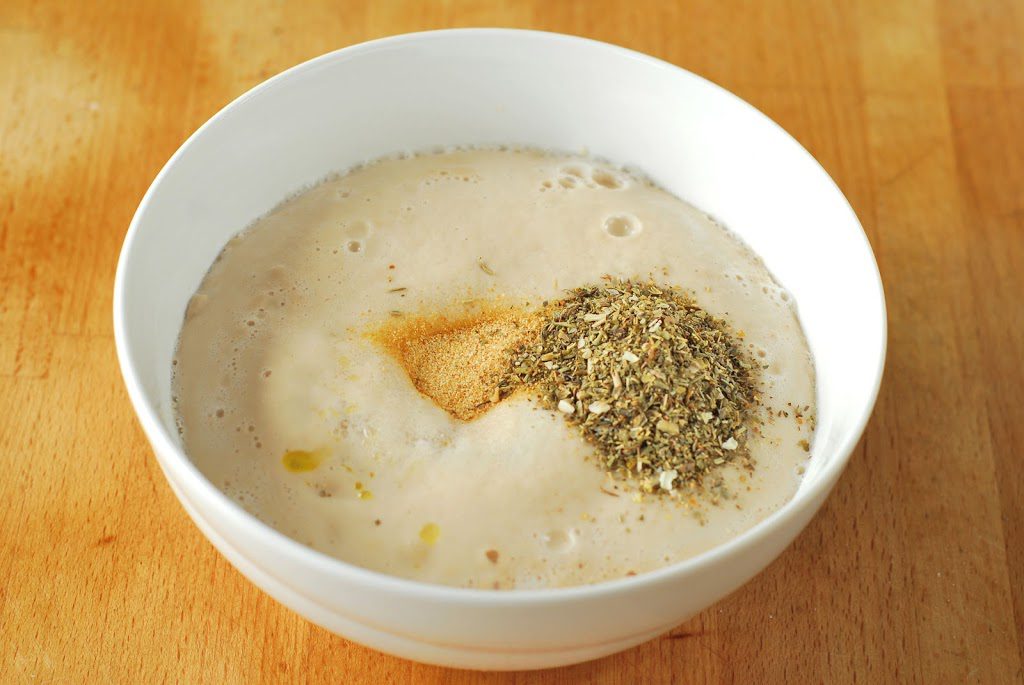 Proofed yeast with salt, olive oil, garlic powder, and Italian seasoning in white bowl