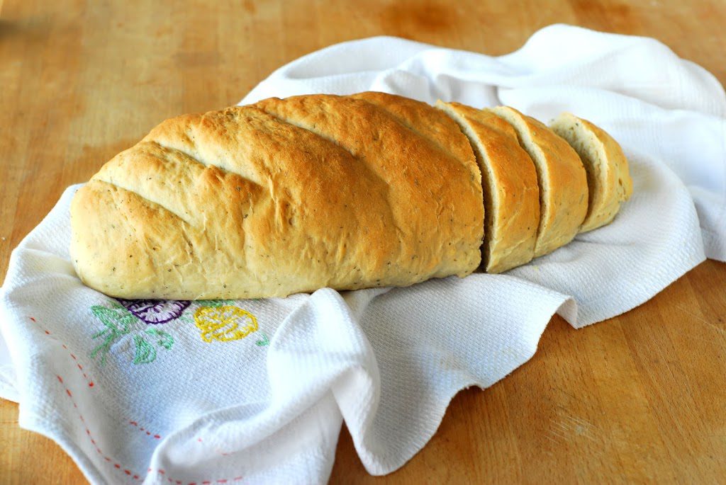 Sliced loaf of bread on white tea towel on wood surface