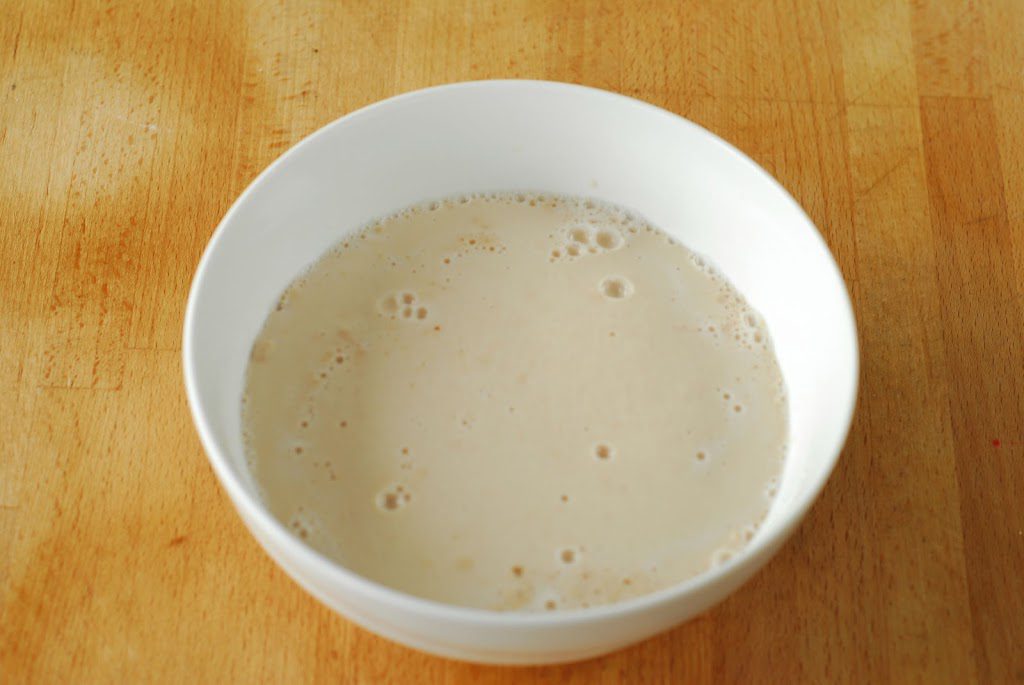 Yeast proofing in white bowl on wood surface