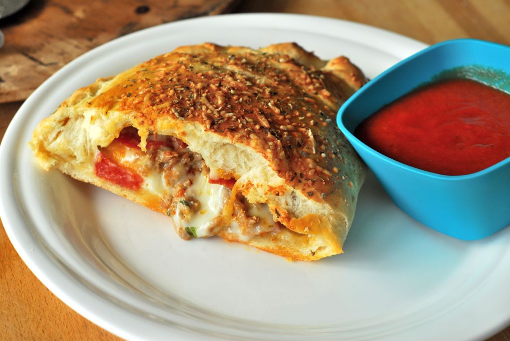 Calzone on white plate with blue bowl of pizza sauce