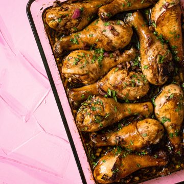 Chicken legs in balsamic sauce in glass baking dish on pink surface