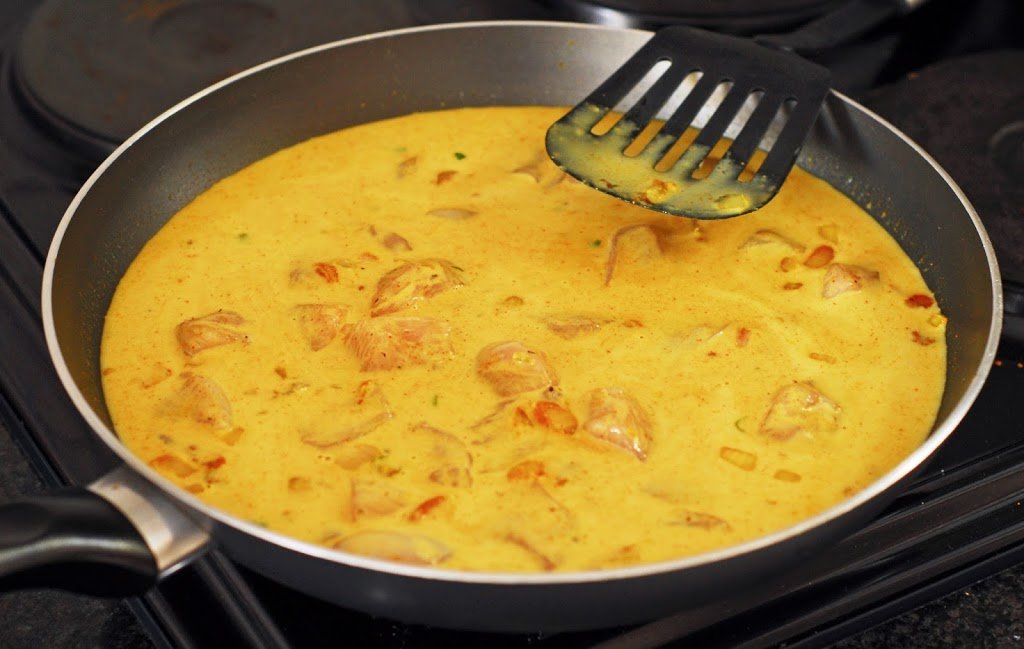 Raw chicken and pineapple curry in saute pan.