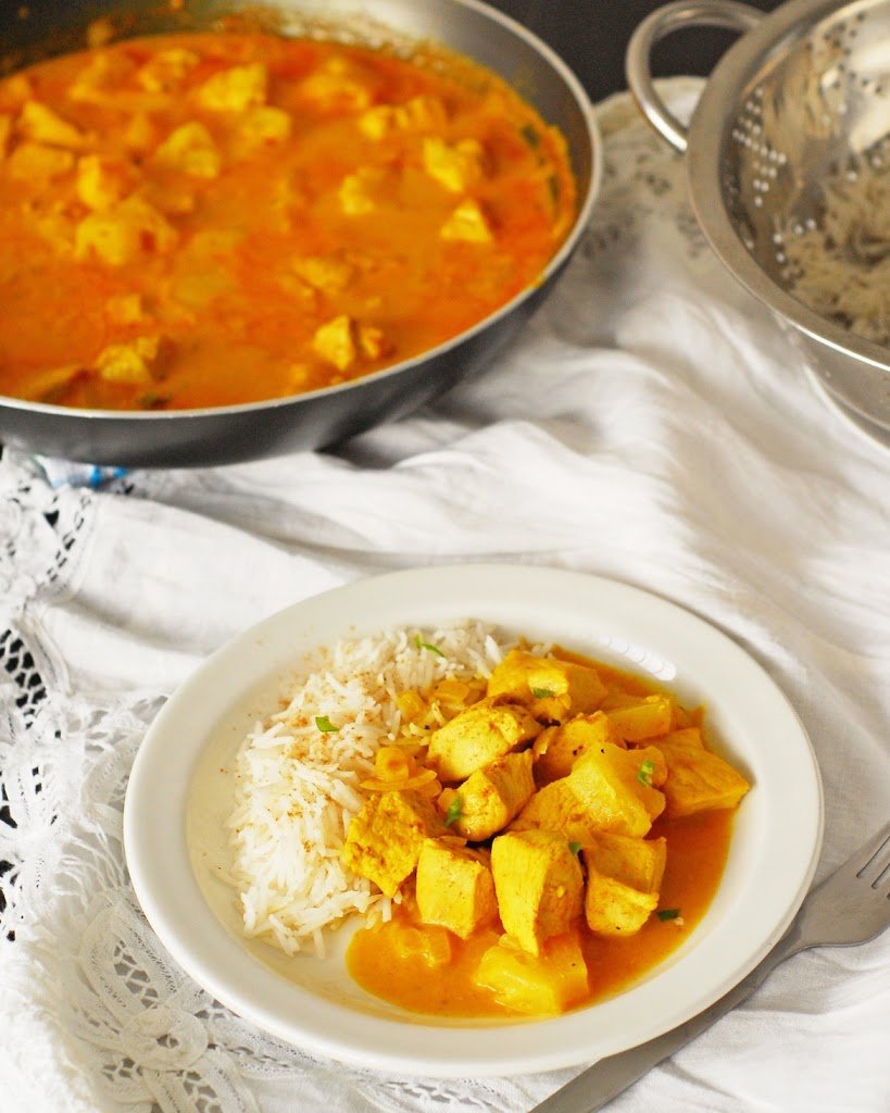 Chicken and pineapple curry and basmati plate on a white plate with skillet in background.