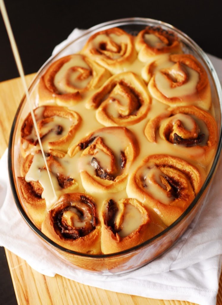 Bacon cinnamon rolls in glass baking dish with icing being poured on