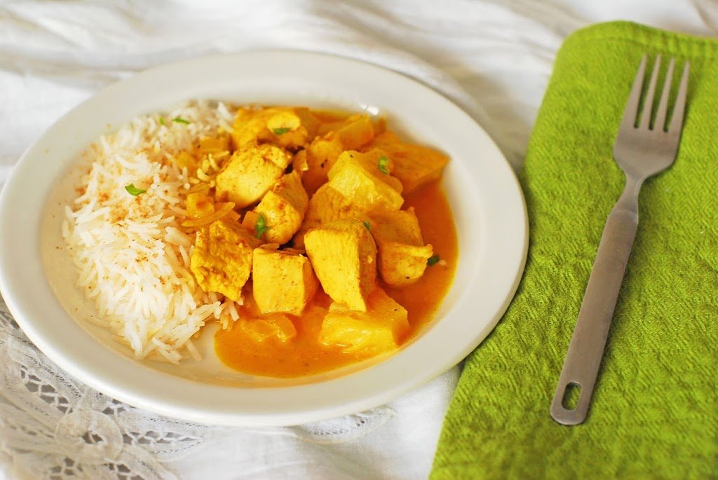 Chicken and pineapple curry and basmati plate on a white plate with green napkin.