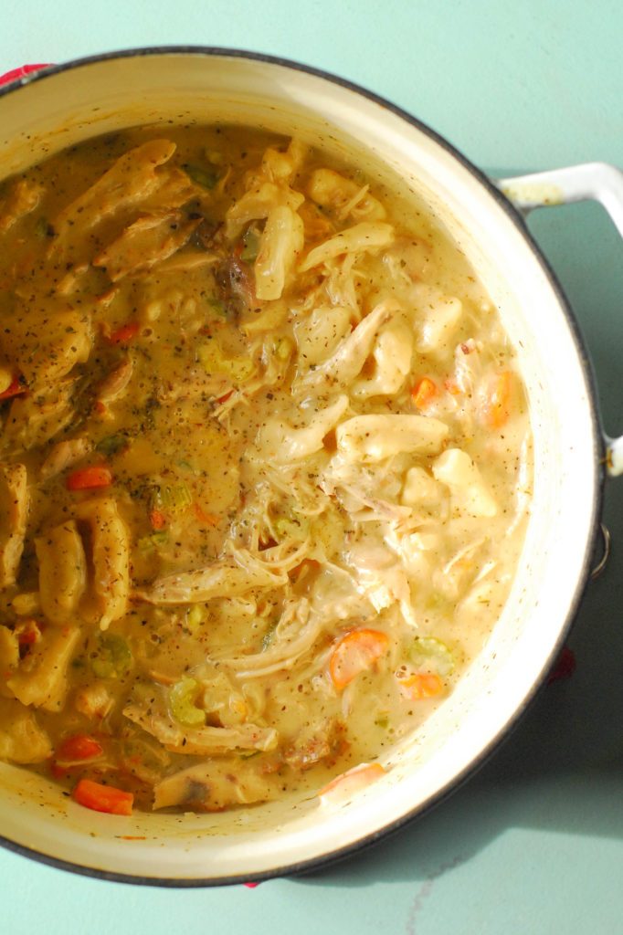 Dutch oven full of chicken and dumplings soup on blue surface