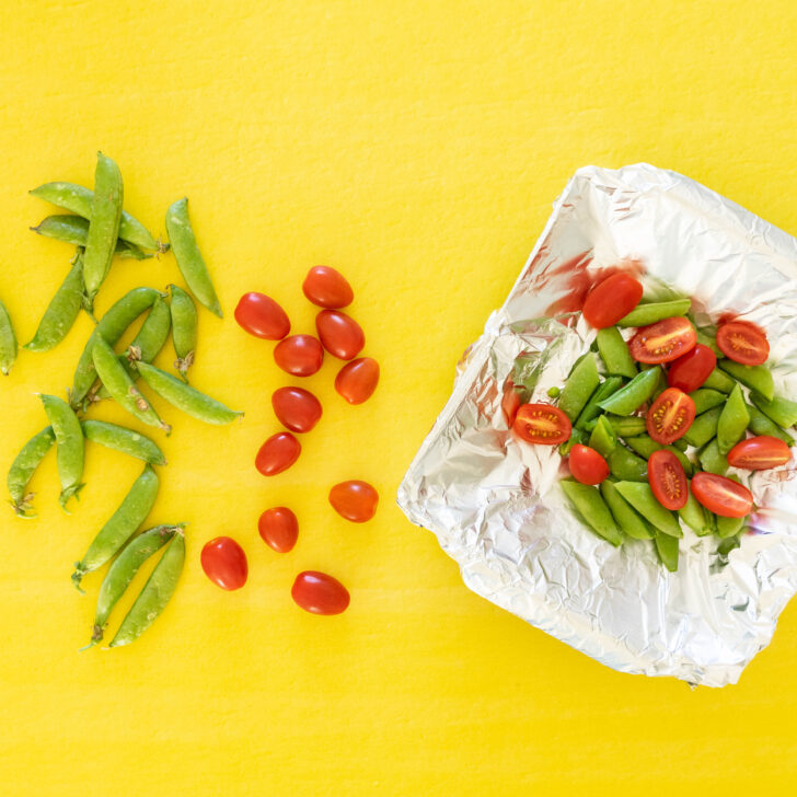 Sugar snap peas and grape tomatoes are arranged on a bright yellow surface; some are whole on the left, while others join a grilled corn salad, halved and mixed in a foil-lined tray on the right.