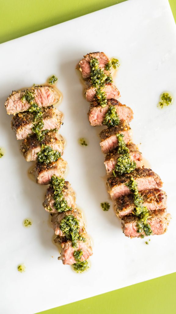  skiver sous vide bøf på en marmor slap på en grøn baggrund med chimichurri sauce spredt over