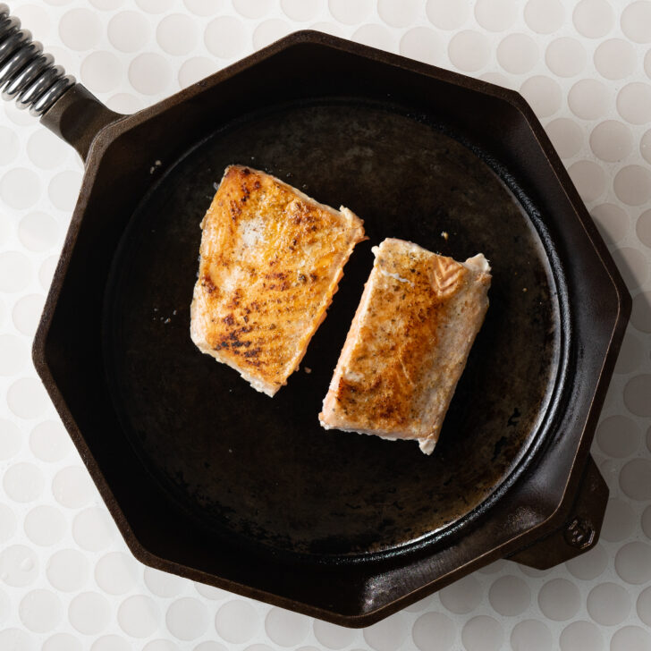 Seared salmon portions in cast iron skillet.