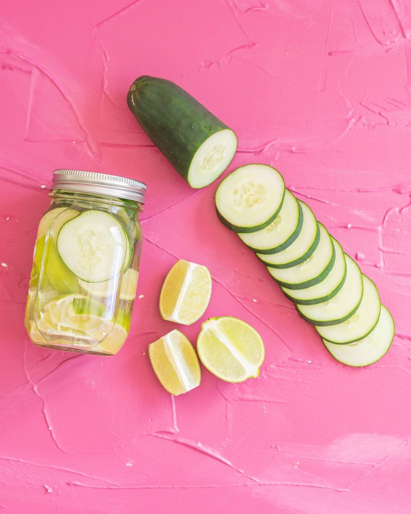 Sous Vide Infused Tequila in a mason jar, next to sliced cucumbers and lemons