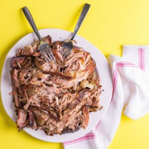 shredded sous vide pork on a white plate and yellow background