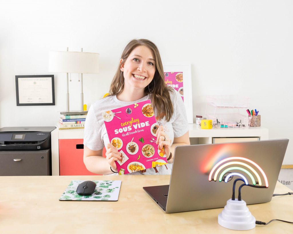 Chelsea holding her cookbook while sitting at her desk.