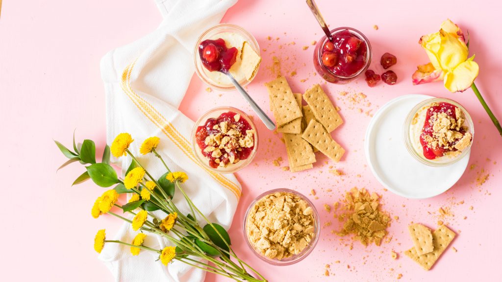 Individual sous vide cheesecakes in glass jars arranged on a pink background