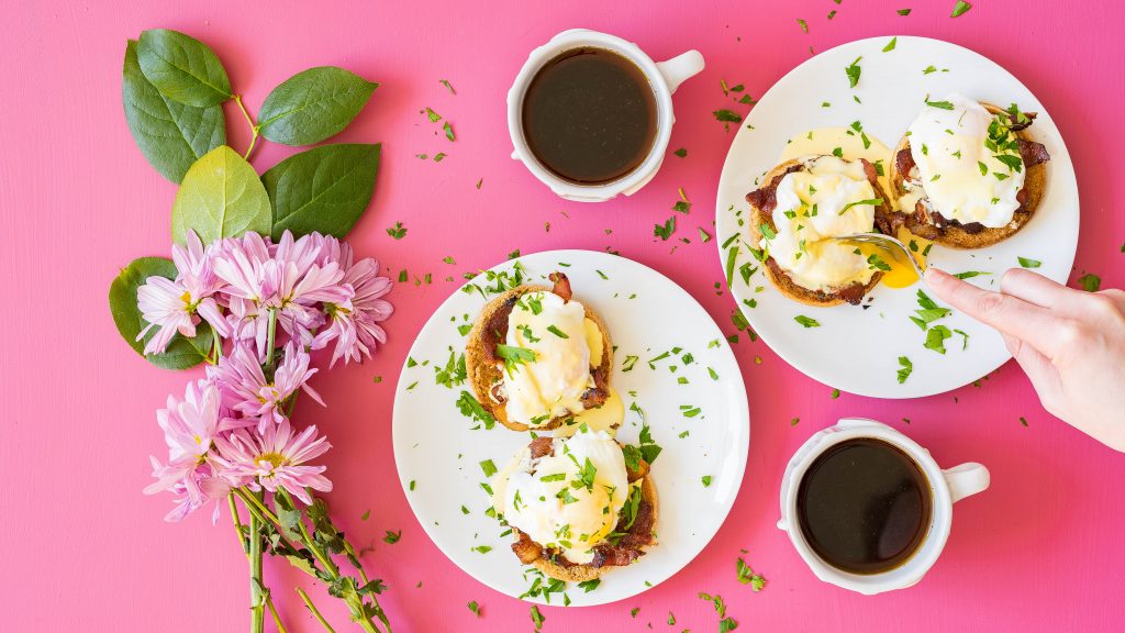 Sous vide hollandaise sauce on breakfast sandwiches arranged on a pink background