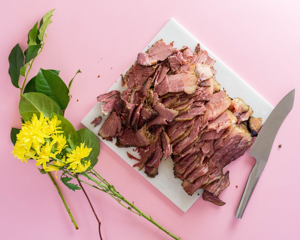 Sliced pastrami on a marble slab with flowers and a pink background.