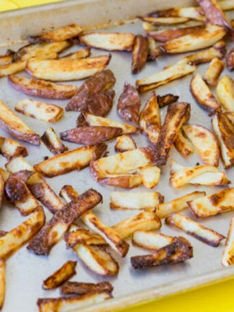 A baking sheet filled with golden-brown, crispy oven fries, spread out in a single layer, sits on a bright yellow surface.