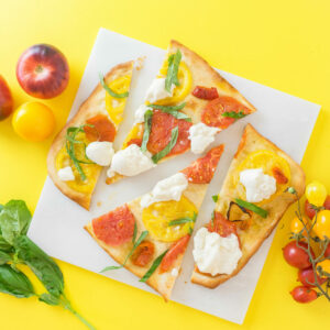 Flatbread with tomatoes and burrata cut into pieces on a marble slab