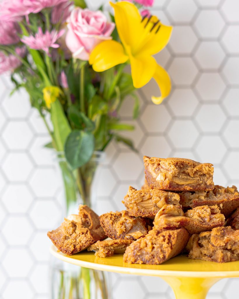 Brown Butter Apple Blondies on a yellow cake stand with flowers and hexagon tile in the background