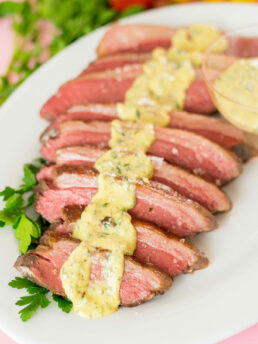 Sliced beef on a platter with parsley and horseradish dijon sauce spooned over the meat.