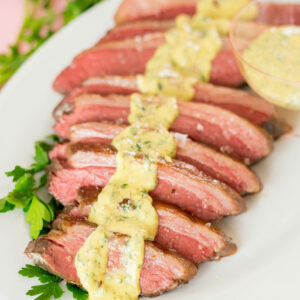 Sliced beef on a platter with parsley and horseradish dijon sauce spooned over the meat.