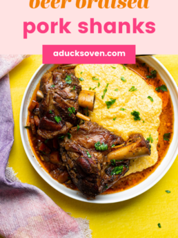 Beer braised pork shanks served with cheddar grits in a white bowl.