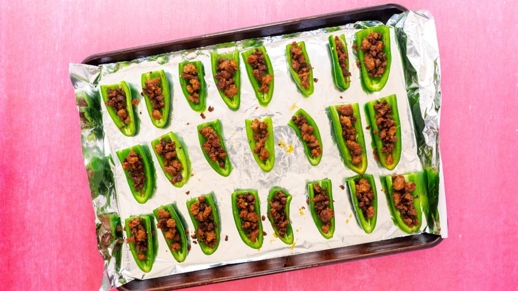 Tray of sliced in half jalapenos filled with chorizo on pink surface