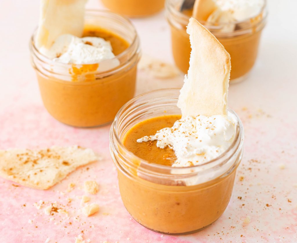 Jars of pumpkin pie with pieces of crust on pink surface