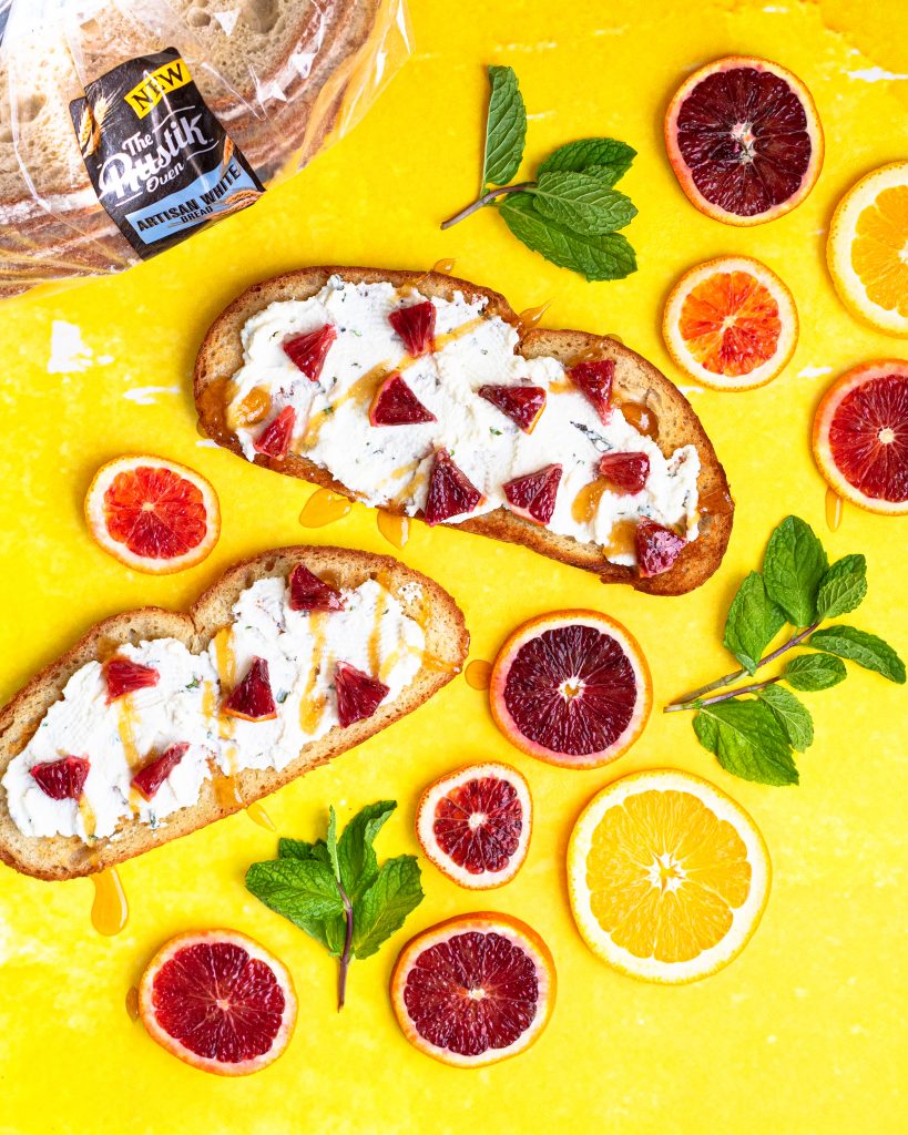 Blood Orange and Mint Ricotta Toast on yellow backdrop with Rustik oven bread in background