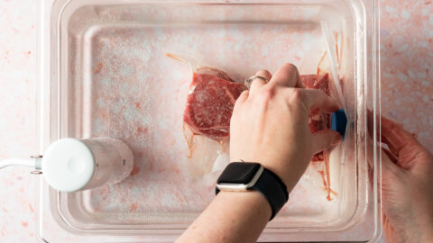 Securing vacuum sealed filet mignon with sous vide magnets in sous vide water bath.