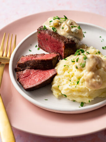 Sous vide filet mignon with blue cheese gravy and mashed potatoes on white and pink plates.