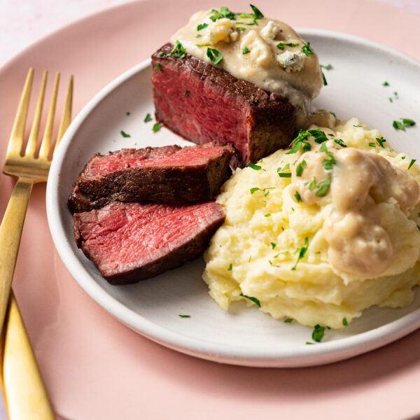 Sous vide filet mignon with blue cheese gravy and mashed potatoes on white and pink plates.
