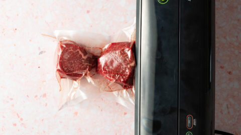 Filet mignon being vacuum sealed on pink surface.