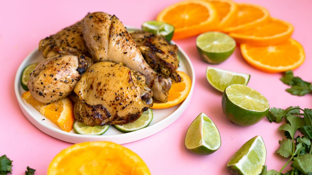 Mojo chicken on a white plate on a pink surface with cut up oranges and limes