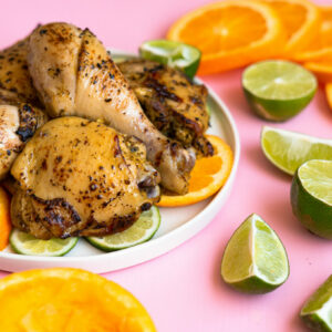 Mojo chicken on a white plate on a pink surface with cut up oranges and limes