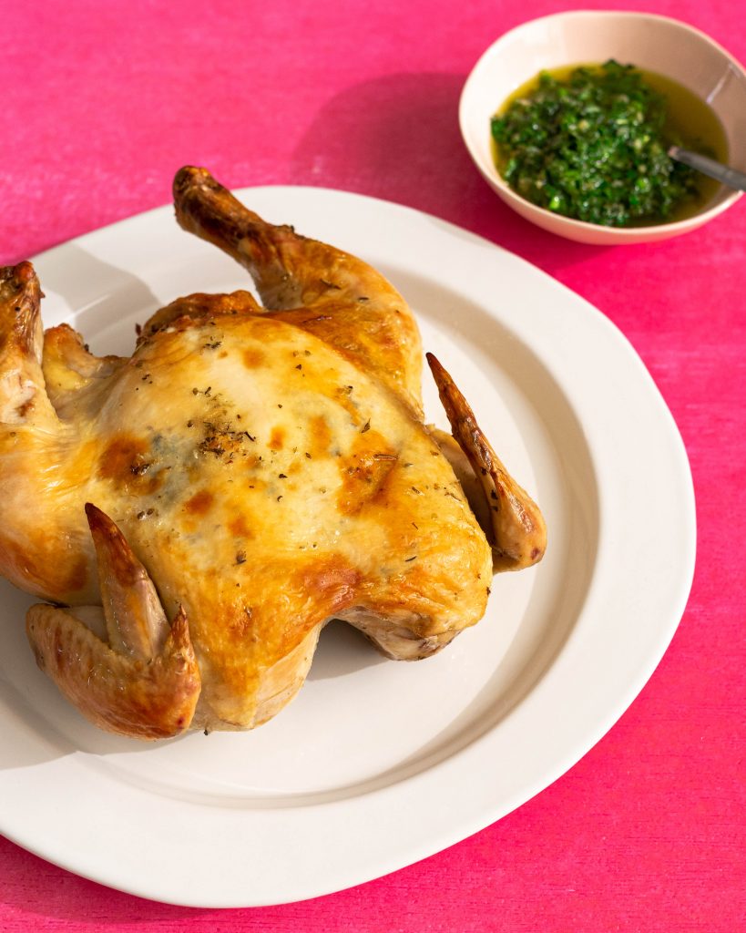 Cooked whole chicken on white plate on pink background