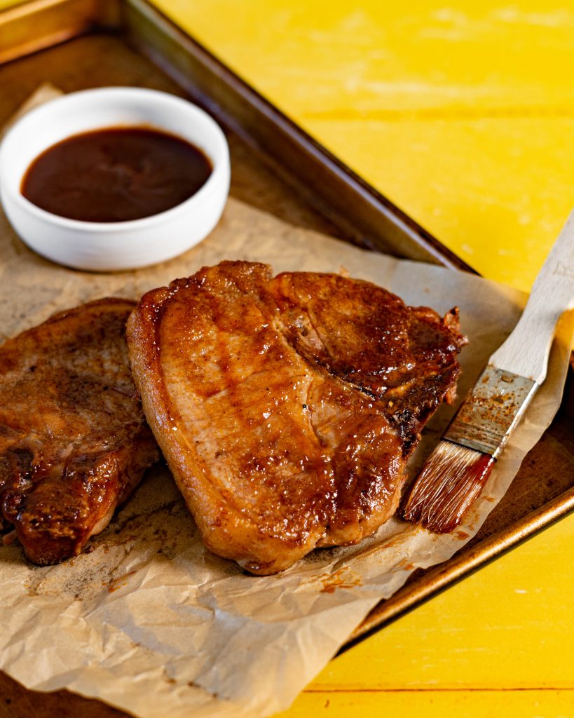 Bone-in pork chops smothered with BBQ Sauce on cookie sheet