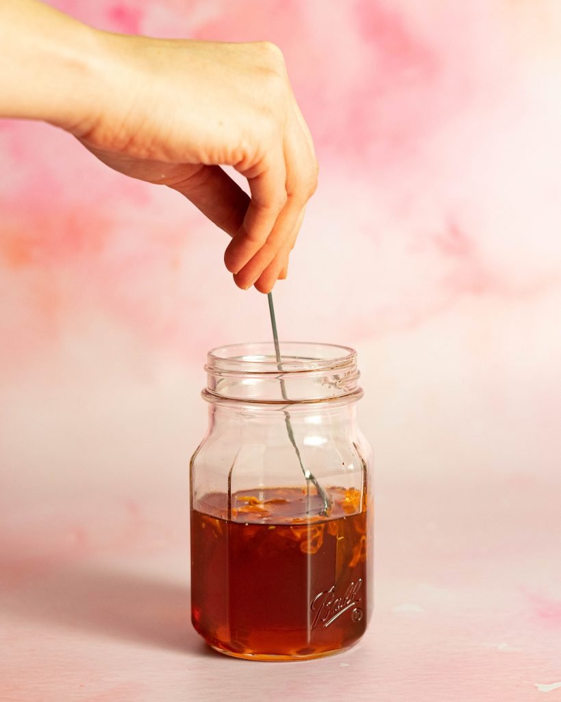 Hand stirring jar of honey on pink and orange background