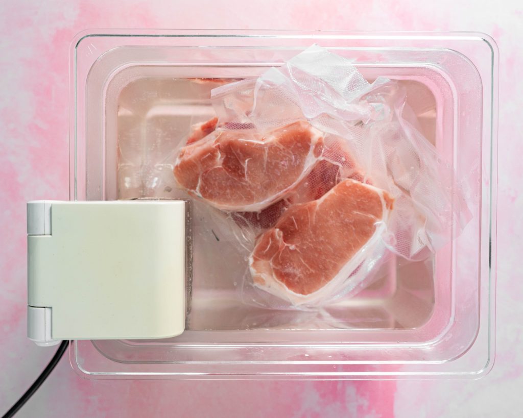 Vacuum sealed pork chops in water bath on pink surface