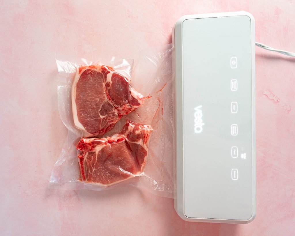 Pork chops being vacuum sealed on pink surface