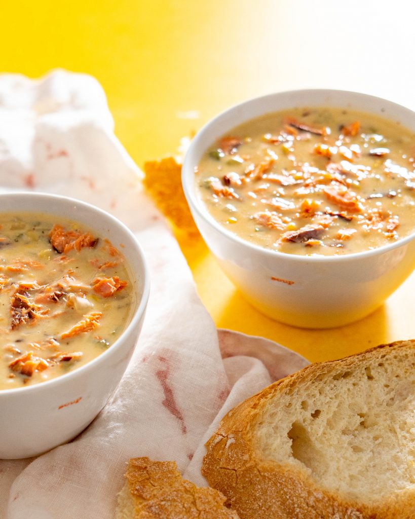 Two bowls of salmon chowder and crusty bread on a yellow surface.