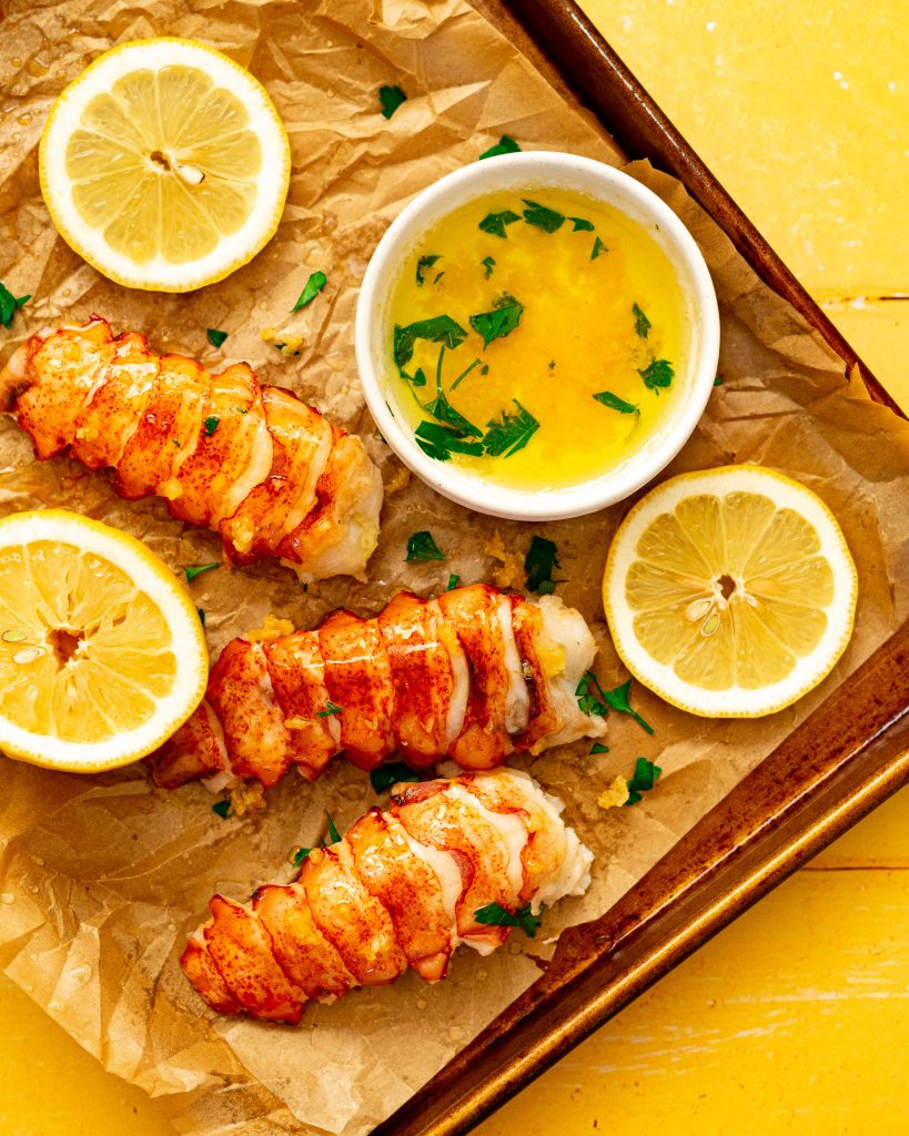 Sous vide lobster tails on baking sheet with lemons and bowl of garlic butter