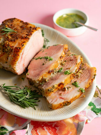 Sliced pork tenderloin roast on platter on pink surface