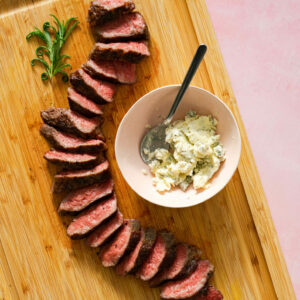 Sliced tri-tip and bowl of blue cheese butter on wood cutting board