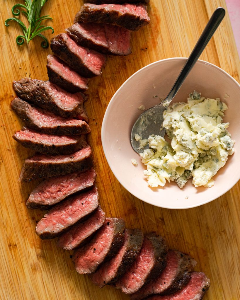 Sliced tri-tip and bowl of blue cheese butter on wood cutting board