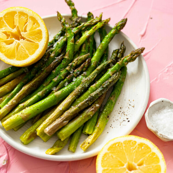 Asparagus spears on a white plate with lemons on a pink surface