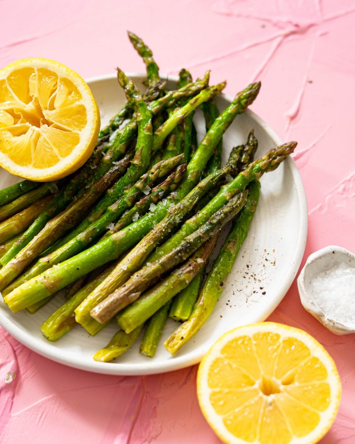 Asparagus spears on a white plate with lemons on a pink surface
