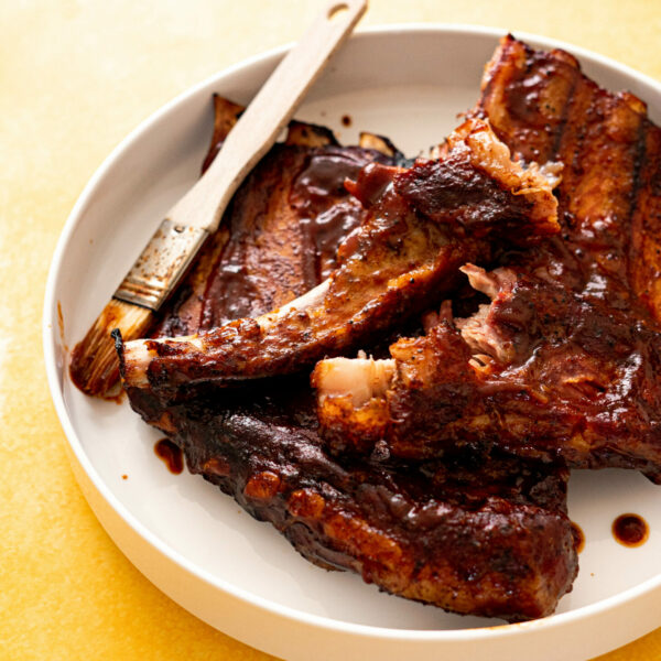 Ribs brushed with BBQ sauce on white platter on yellow surface