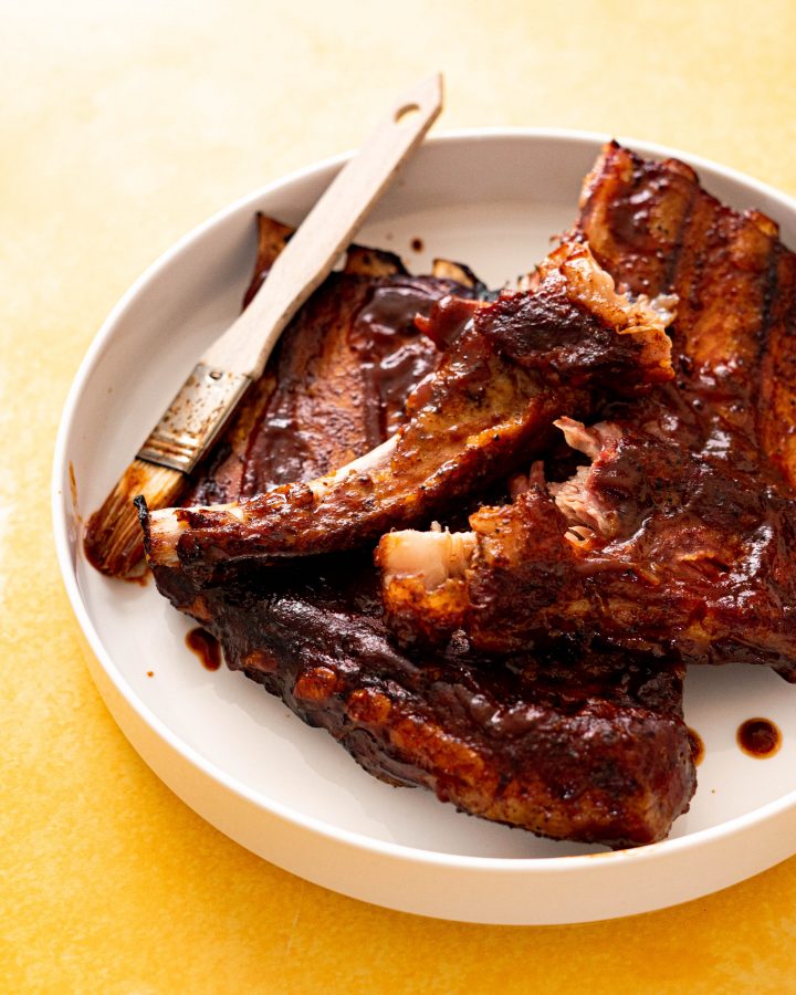 Ribs brushed with BBQ sauce on white platter on yellow surface